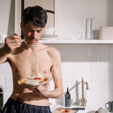 Young man enjoying a breakfast omelette in a sunlit kitchen setting.